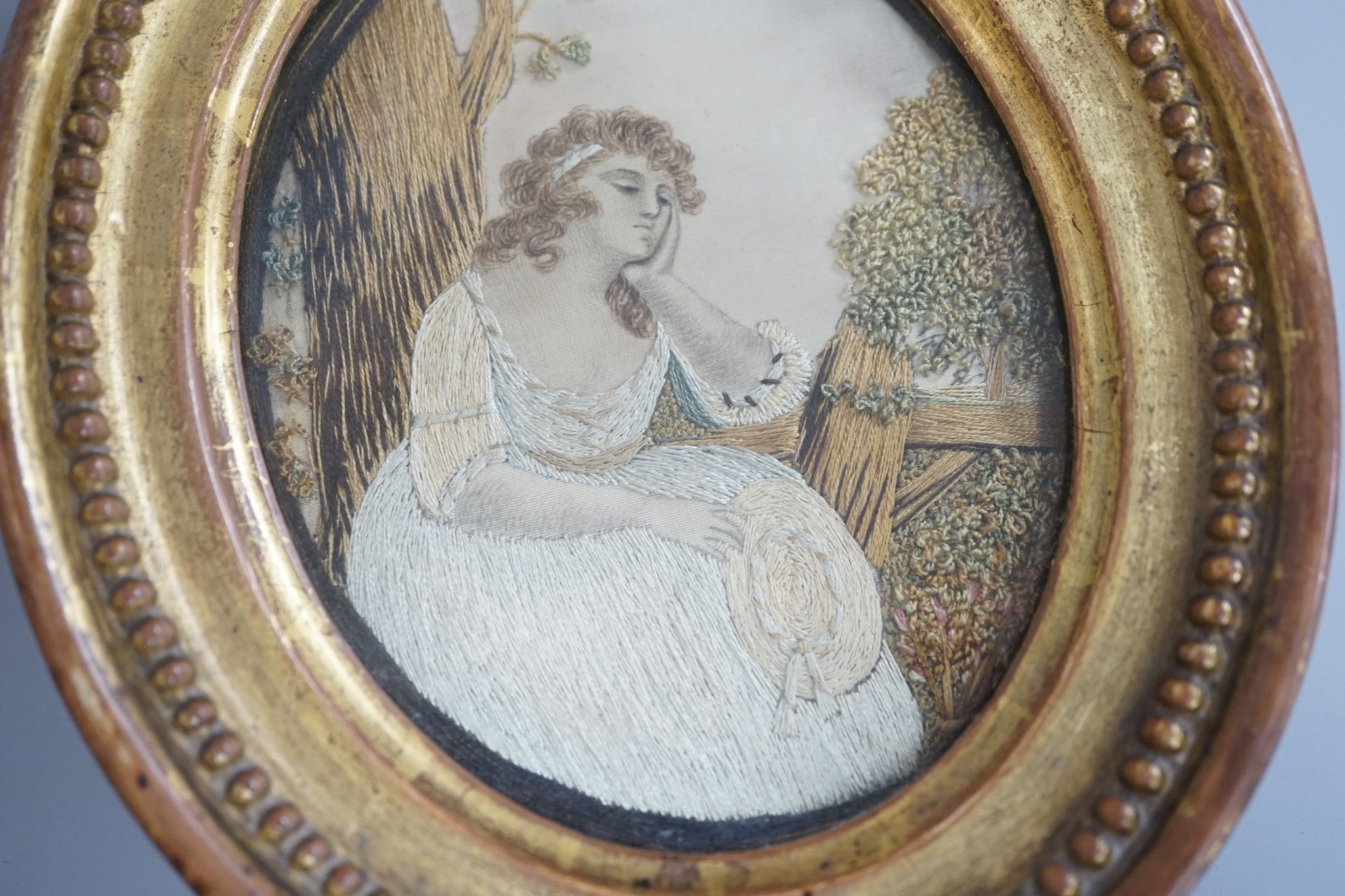 An oval gilt framed Regency silkwork of a seated girl 11x9cm